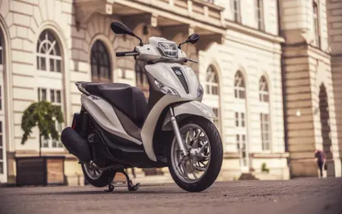 Biały skuter Piaggio Medley zaparkowany na bruku przed zabytkową kamienicą.