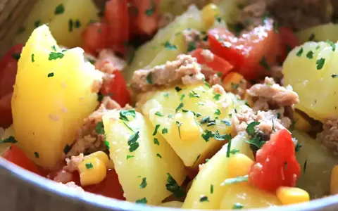Salade de pommes de terre, thon, tomates et maïs, parsemée de persil frais. Un plat simple et savoureux.