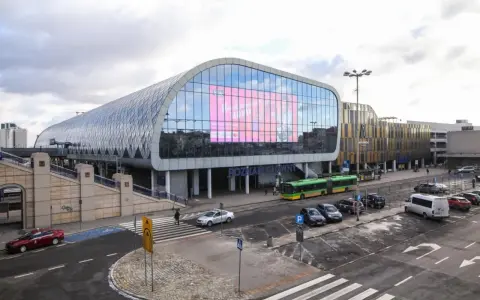 Nowoczesny Poznań Główny z charakterystyczną szklaną fasadą i ekranem. Autobusy i samochody czekają na pasażerów.