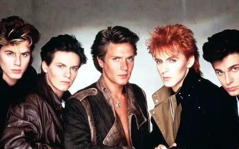 Fünf Männer mit auffälligen Frisuren und 80er-Jahre-Mode, die an ikonische Musikvideos dieser Ära erinnern.