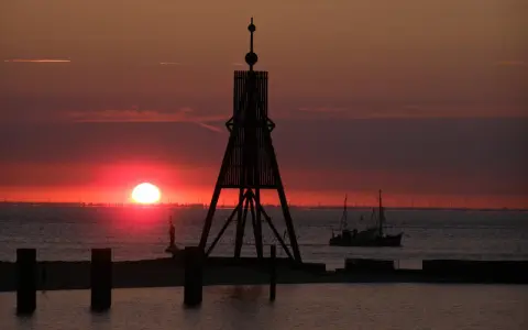 Sonnenuntergang in Cuxhaven: Ein Leuchtfeuer und ein Fischerboot auf dem Meer. Hier kann man die Weite genießen und den Tag ausklingen lassen.