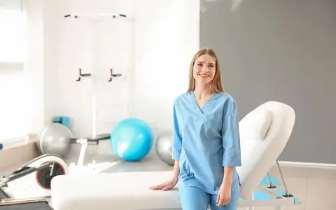 Uśmiechnięta fizjoterapeutka w gabinecie rehabilitacyjnym. Zastanawiasz się, ile zarabia fizjoterapeuta?