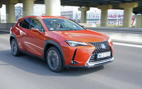 Pomarańczowy Lexus UX 250h jedzie po miejskiej drodze pod wiaduktem.