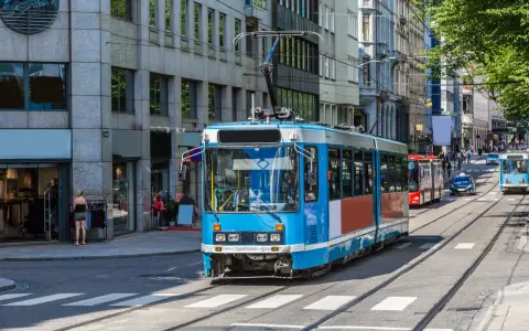 Błękitny tramwaj na tle budynków w Oslo. To część sprawnie działającej oslo komunikacji miejskiej, która przewozi mieszkańców i turystów.