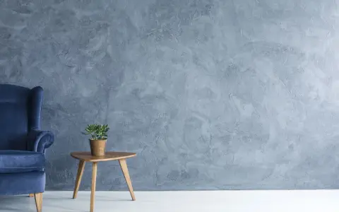 Fauteuil bleu profond devant un mur texturé avec une peinture effet stucco. Une petite table en bois supporte une plante verte.