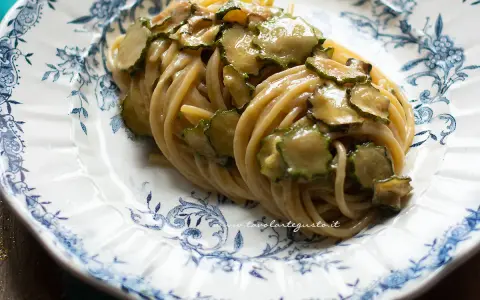 Un piatto di spaghetti alla nerano ricetta, conditi con zucchine saltate e una cremosa salsa al formaggio, serviti su un piatto decorato.
