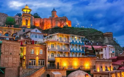 Tbilisi co zobaczyć: malownicze, oświetlone kamienice i twierdza Narikala na wzgórzu o zmierzchu.