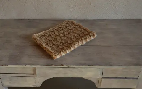 En vacker babyfilt stickad i ett vågmönster med ljusa och mörkare bruna nyanser.