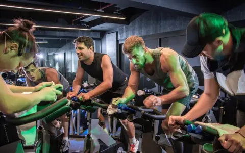 Intensywny trening spinningowy w grupie. Ludzie z determinacją pedałują na rowerach stacjonarnych, pocą się i walczą o każdy kilometr.