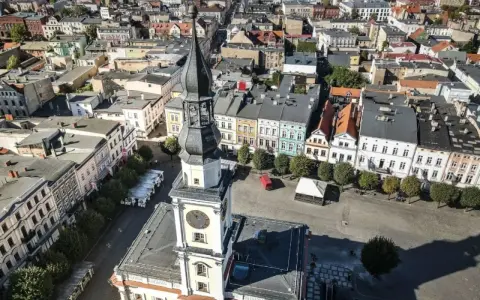 Widok z lotu ptaka na rynek w Lesznie. Wieża ratusza góruje nad kolorowymi kamienicami, ukazując urokliwe leszno atrakcje.