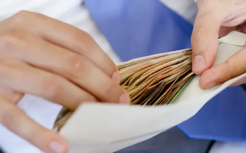 Dłonie wkładają plik banknotów do koperty na wesele.