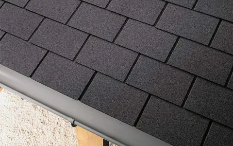 Détail d'une toiture en pose de bardeau bitumé gris foncé, avec une gouttière grise.