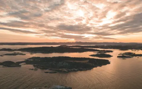 Zachód słońca nad archipelagiem, przypominającym szwedzkie fiordy. Woda odbija złote światło, a chmury malują niebo.