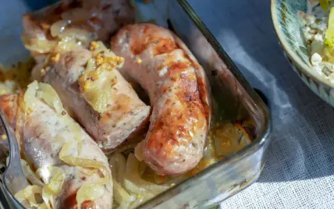 Soczysta biała kiełbasa pieczona z cebulką i musztardą, podana w szklanym naczyniu.