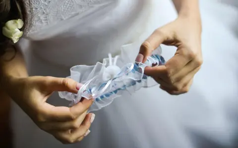 Braut hält ein weißes Strumpfband mit blauen Akzenten. Das Strumpfband ist ein traditionelles Symbol für Glück bei der Hochzeit.