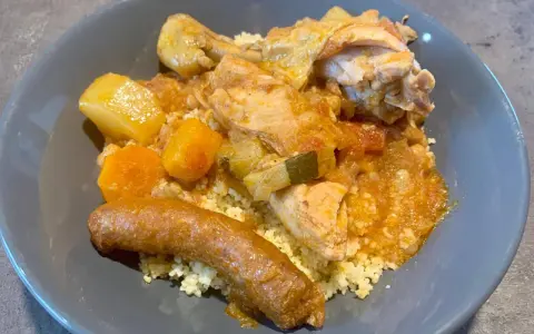 Un plat appétissant de tajine poulet merguez, servi sur un lit de semoule, avec des morceaux de poulet, des légumes et une merguez dorée.