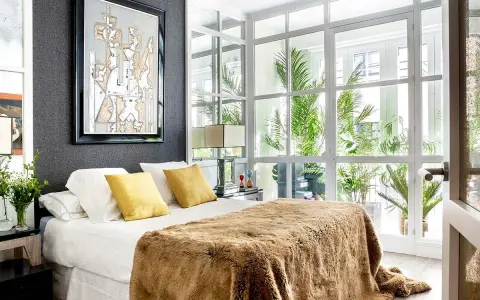 Un dormitorio moderno con cama mullida, arte abstracto y ventanales que invitan a diseña tu dormitorio con luz natural y plantas.