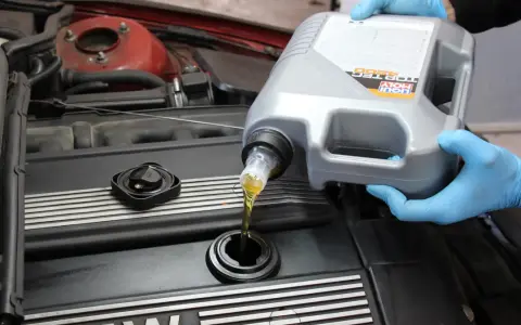 Ręce w niebieskich rękawiczkach wlewają olej silnikowy Liqui Moly do silnika. Czy można mieszać oleje silnikowe? To pytanie nurtuje wielu kierowców.