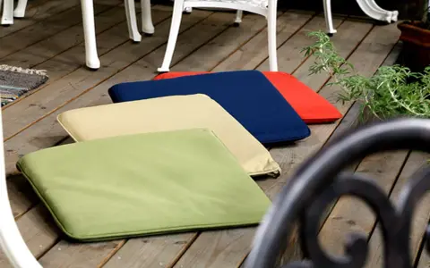Mehrere bunte gartenpolster nass geworden, liegen auf einer Holzterrasse neben Gartenmöbeln.