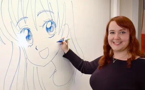 En kvinna med rött hår ritar en stor manga teckning på en whiteboard.