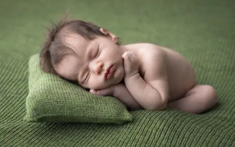 Dolce neonato scatti nel sonno, appoggiato su un cuscino verde. La sua manina è vicino al viso, in un sonno profondo e sereno.