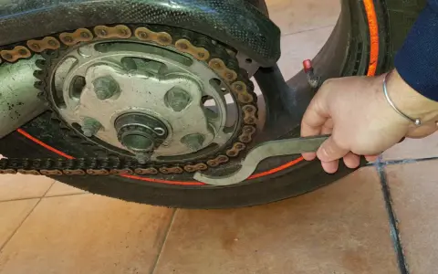 Mano con chiave speciale per regolare la catena della moto, mostrando come tirare la catena.