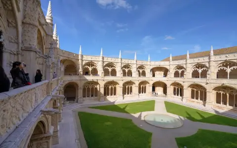 The Jerónimos Monastery, a stunning monastery in Portugal, features a grand courtyard with intricate stonework and a lush green lawn.