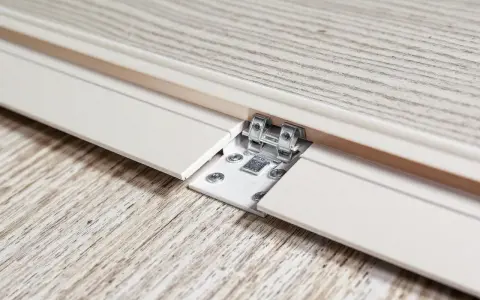 Détail d'une lame PVC qui se soulève, révélant une fixation métallique et des vis sur un parquet imitation bois.