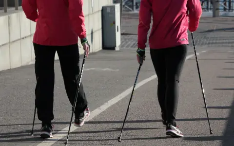 Dwie osoby w czerwonych kurtkach i czarnych spodniach maszerują z kijki do nordic walking.