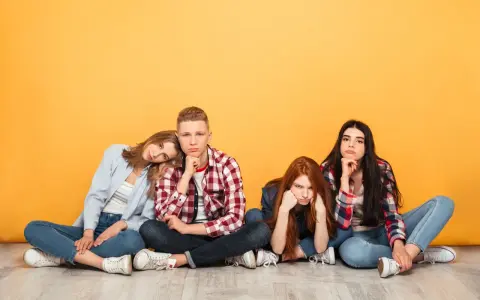 Vier junge Leute sitzen auf dem Boden, die Gesichter zeigen deutliche Langeweile.