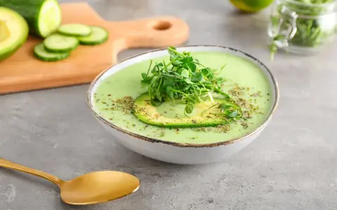Gazpacho de aguacate cremoso con rodaja de aguacate y brotes verdes, servido en un cuenco blanco.