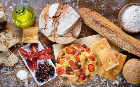 Apulia jedzenie: świeże pieczywo, focaccia z pomidorami, oliwki, suszone pomidory i oliwa z oliwek na drewnianym stole.