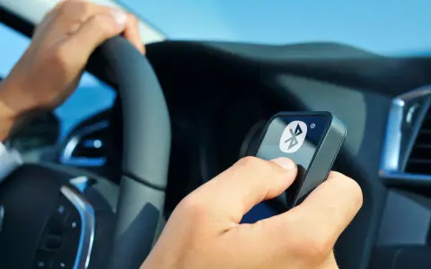 Fahrer hält ein Gerät mit Bluetooth-Symbol, während er das Lenkrad en 300 328 bedient.