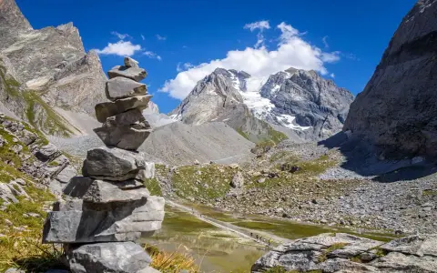 Un cairn, une pile de pierres, marque le chemin dans un paysage de montagne spectaculaire, avec un glacier au loin.