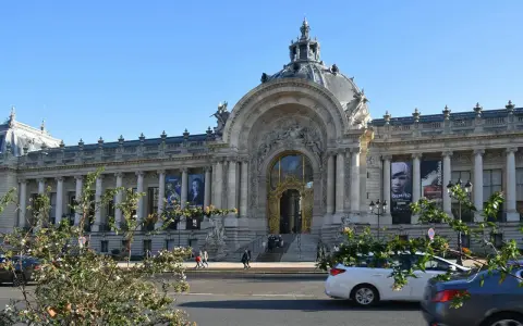El Petit Palais, un edificio majestuoso con una cúpula y una entrada dorada, exhibe carteles de arte bajo un cielo azul.