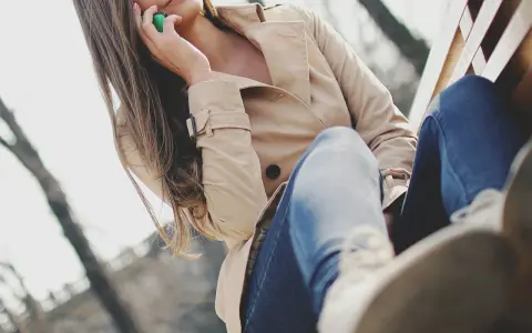 Kobieta w beżowym płaszczu z lumpeksu rozmawia przez telefon, siedząc na ławce. Jak wyczyścić płaszcz z lumpeksu?