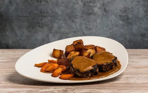 Delicioso rabo de toro bañado en salsa, acompañado de patatas rústicas y zanahorias glaseadas.