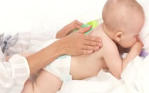 Delikatny masaż pleców niemowlaka, który waży już 9 kg. Ręce opiekuna głaszczą jego plecy.
