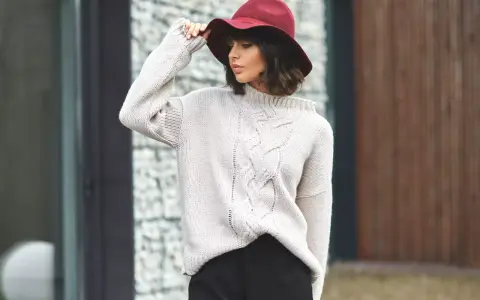 Elegancka kobieta w bordowym kapeluszu i beżowym swetrze z warkoczami. Stylowe sukienka i sweter stylizacje na chłodniejsze dni.