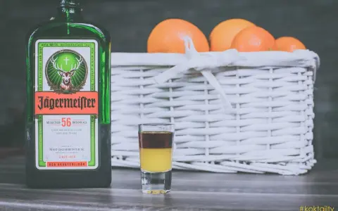 Butelka Jägermeistera i shot z dwoma warstwami, obok koszyk z pomarańczami. Idealne na wieczór, jak pić jagermeister.