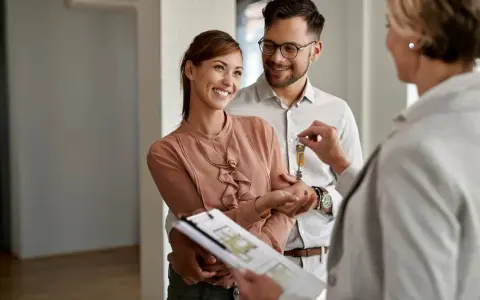 Pareja feliz recibe las llaves de su nuevo hogar, con un agente inmobiliario mostrando las escrituras de una casa.