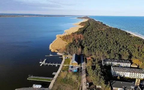 Dąbki atrakcje: malowniczy widok na jezioro, las, plażę i budynki. Widoczne molo, przystań jachtowa i zabudowania.