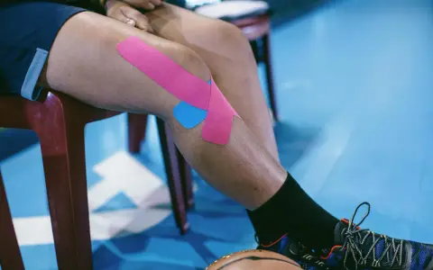 Sportowiec z plastrami na kolanie, przygotowujący się do ćwiczeń na chondromalację rzepki.