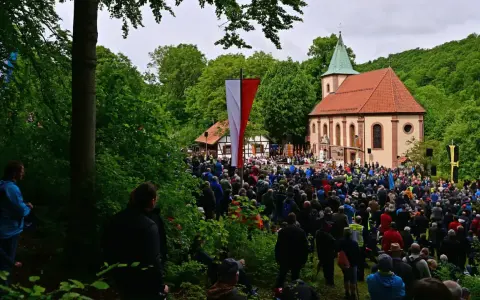 Große Menschenmenge versammelt sich vor einer Kirche zu Christi Himmelfahrt. Fahnen wehen, ein Gottesdienst findet statt, inspiriert von der Bibel.