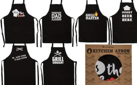 Varios delantales negros con frases divertidas para cocinar y asar: "Kiss the Cook", "Dad is Cooking", "Grill Master", "Insert Beer Here", "Mr. Good Lookin is Good Cookin" y "Grill Sergeant".