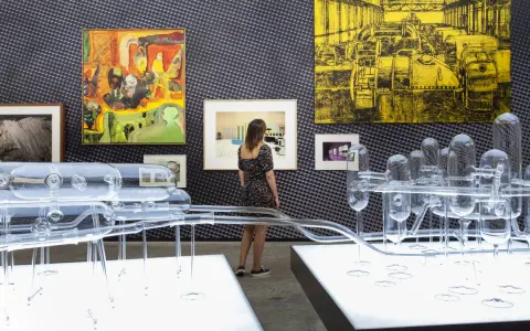 Una curadora de arte observa una instalación de vidrio y pinturas abstractas en una galería.