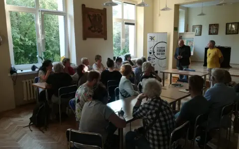 Spotkanie promujące język kaszubski. Ludzie siedzą przy stołach, słuchając prelegentów.