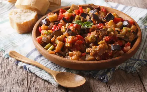 Un plat de caponata, une recette sicilienne savoureuse, garni de basilic frais, servi avec du pain croustillant.