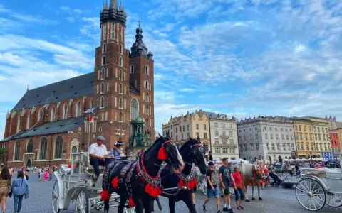 Horse-drawn carriages await tourists in Krakow's Old Town, a picturesque scene from a Poland trip, with St. Mary's Basilica towering in the background.