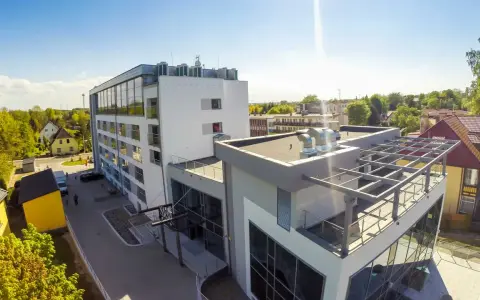 Nowoczesny budynek, gdzie hotel skal właściciel dba o komfort gości. Widać parking, zielone otoczenie i słoneczne niebo.